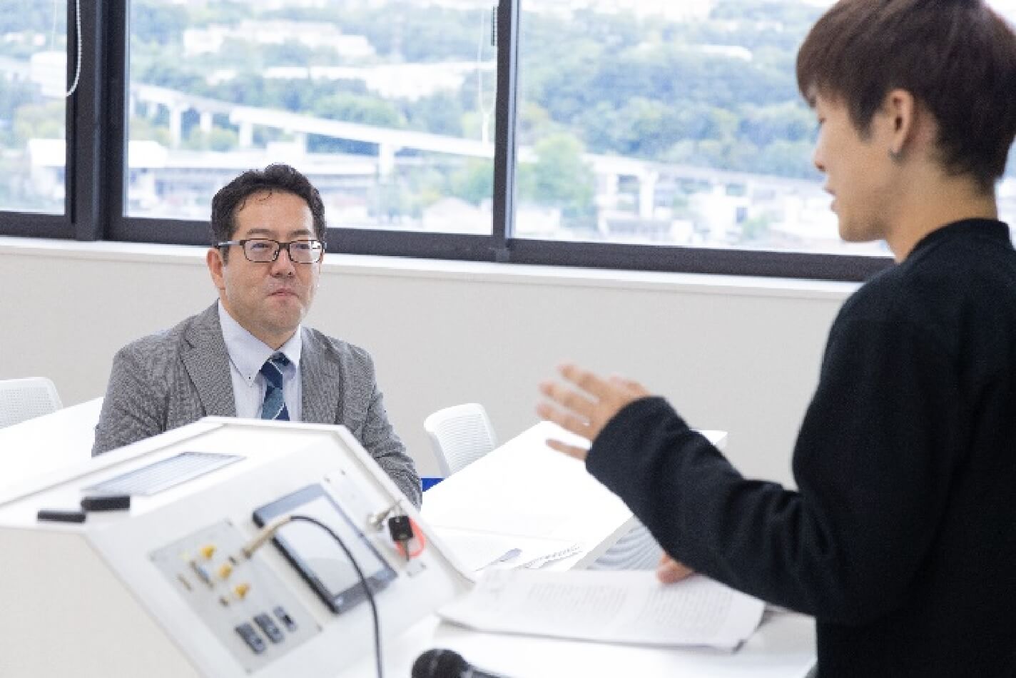 小山俊樹教授が男性生徒と会話をしている様子