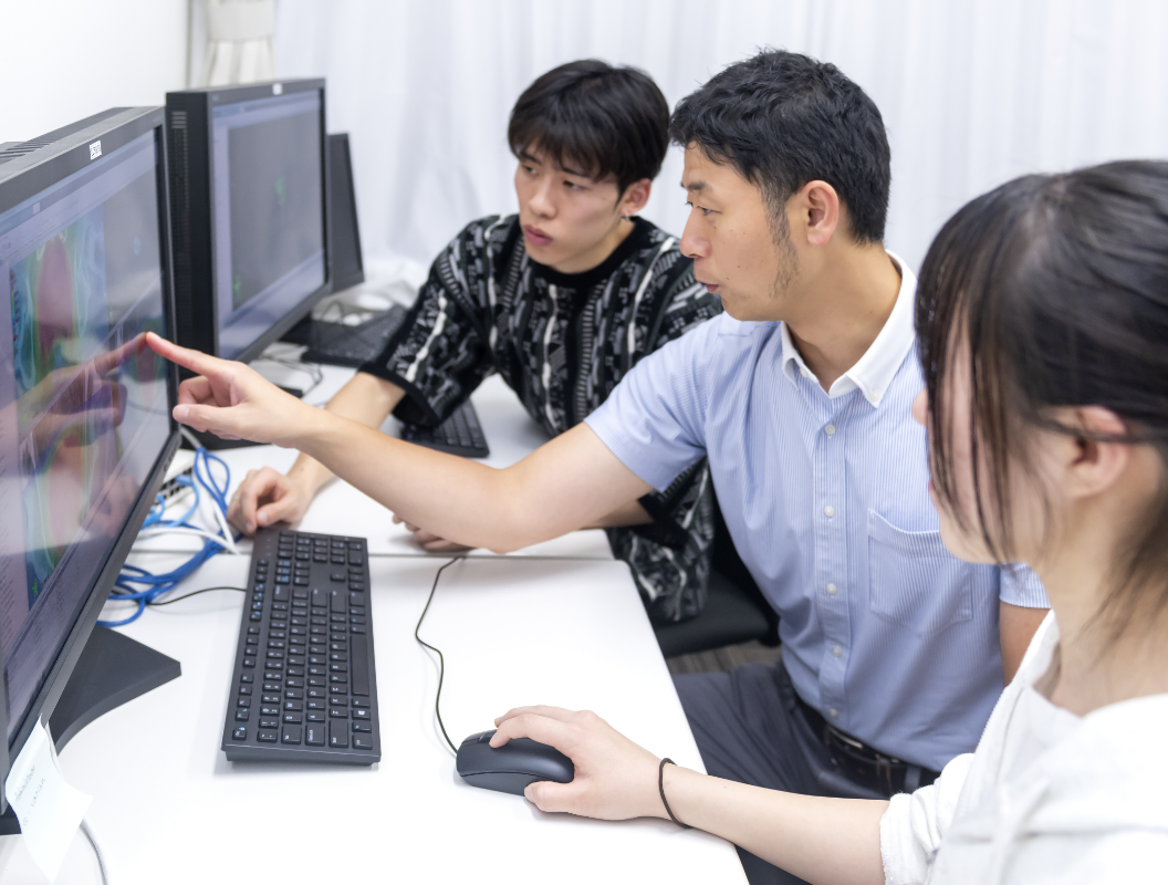亀澤准教授がパソコンを指さしながら、生徒たちに教えている様子